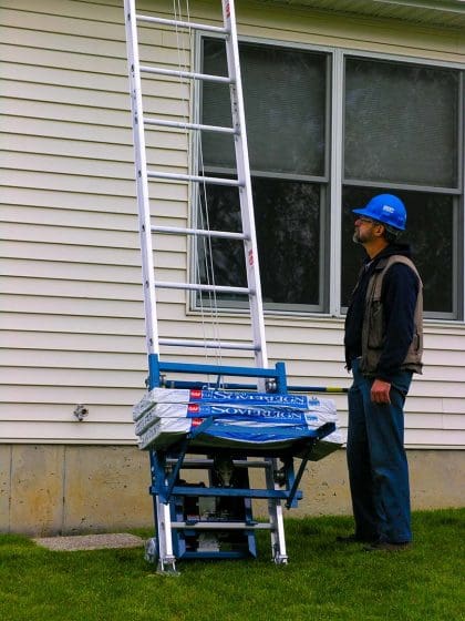 Man operating Ladder Hoist lifting roofing materials.